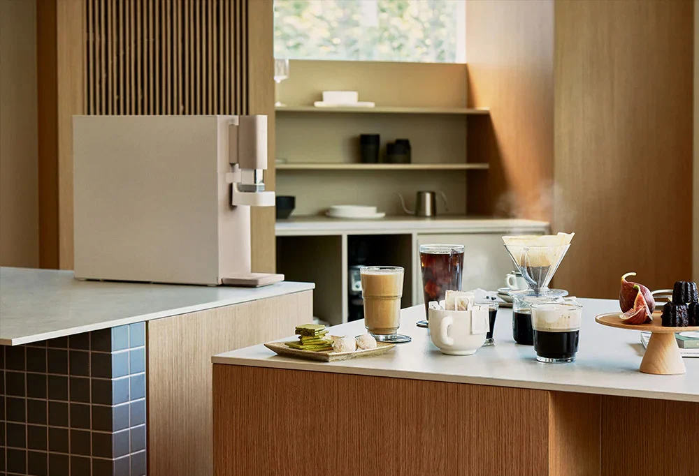 现代厨房台面上的 CUCKOO STEAM 100 Barista 净水器与咖啡饮品,配有宣传文字。(cp-abnc100)