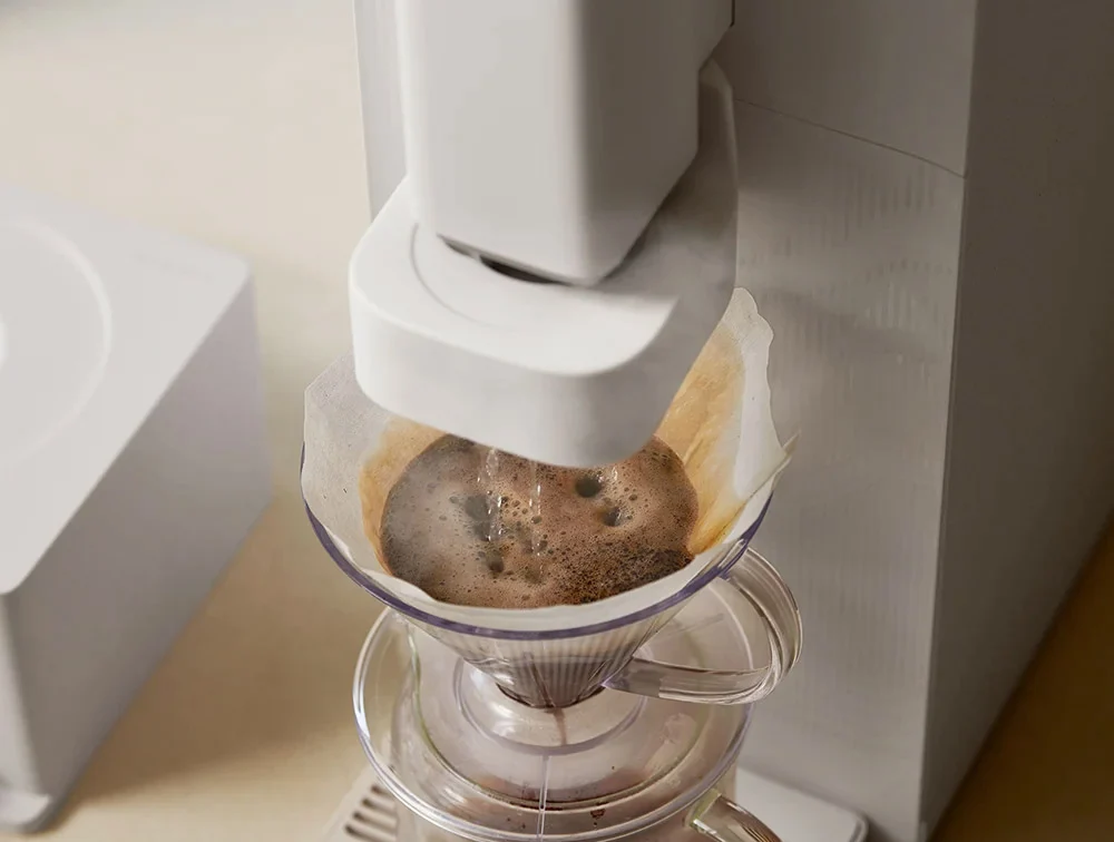 STEAM 100 Barista 净水器将刚冲好的咖啡滴入玻璃咖啡壶的特写,锥形滤座中放有白色滤纸。